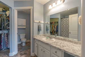 Full bath featuring a textured ceiling, a walk in closet, vanity, and dark stone finish floors