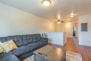 Living room with a textured ceiling, wood finished floors, electric panel, and ceiling fan