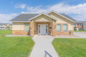 View of front of property with a front yard, stucco siding, stone siding, and roof with shingles