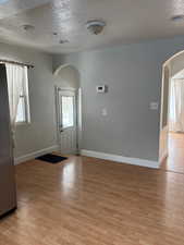 Entrance foyer with arched walkways, a textured ceiling, light wood finished floors, and healthy amount of natural light
