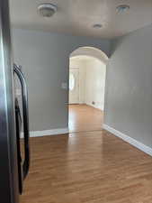 Interior space with arched walkways, freestanding refrigerator, light wood-type flooring, and a textured ceiling