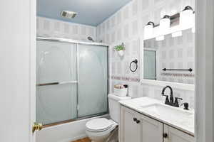 Full bathroom with shower / bath combination with glass door, vanity, and wallpapered walls