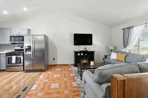 Living room featuring vaulted ceiling, a glass covered fireplace, and light tile patterned flooring