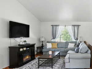 Living room with tile patterned floors, stairway, a glass covered fireplace, a ceiling fan, and vaulted ceiling