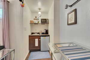 Indoor wet bar with a textured wall, dark wood-style floors, stainless steel appliances, and a textured ceiling