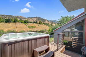 Wooden terrace with a mountain view, a hot tub, and view of scattered trees