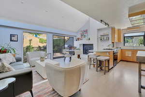 Living room featuring rail lighting, a glass covered fireplace, high vaulted ceiling, and light wood-style flooring