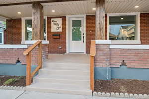 Doorway to property featuring covered porch and brick siding