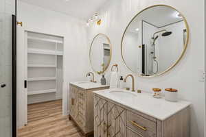 Full bath featuring two vanities, light wood-type flooring, tiled shower, a walk in closet, and recessed lighting