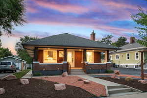 Bungalow-style house with covered porch, brick siding, roof with shingles, and a chimney