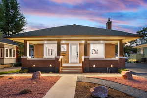 Bungalow-style house with brick siding, a chimney, covered porch, and a shingled roof