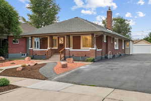 View of front of home featuring brick siding, covered porch, a chimney, a shingled roof, and an outdoor structure