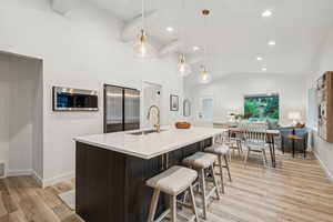 Kitchen with light wood-style flooring, dark brown cabinets, pendant lighting, an island with sink, and recessed lighting