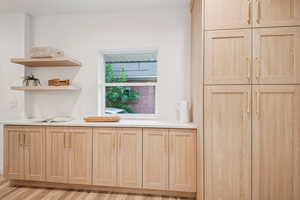 Bar featuring light brown cabinetry, light wood finished floors, light countertops, and open shelves