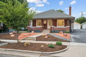 Bungalow with a shingled roof, a porch, an outdoor structure, a garage, and brick siding