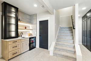 Indoor wet bar with stairway, light carpet, light brown cabinetry, beam ceiling, and beverage cooler