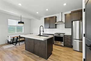 Kitchen featuring decorative light fixtures, stainless steel appliances, wall chimney exhaust hood, tasteful backsplash, and dark brown cabinetry