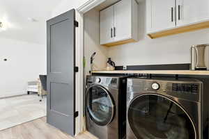 Washroom featuring light wood-style floors, cabinet space, and washer and dryer