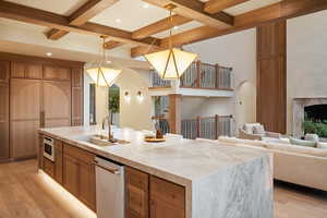 Kitchen with light wood finished floors, brown cabinetry, open floor plan, light stone countertops, and hanging light fixtures