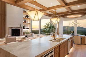 Kitchen with open floor plan, pendant lighting, light wood-type flooring, a fireplace with raised hearth, and beam ceiling