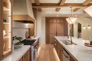 Kitchen featuring light wood-type flooring, light stone countertops, brown cabinetry, appliances with stainless steel finishes, and custom exhaust hood