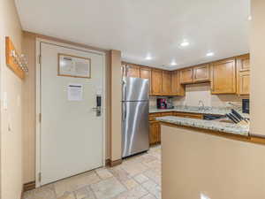 Kitchen featuring light stone counters, freestanding refrigerator, recessed lighting, stone tile floors, and brown cabinets
