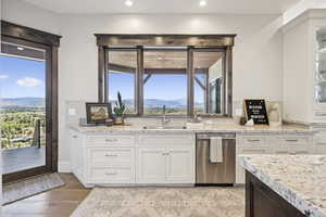 Kitchen with white cabinets, backsplash, light stone countertops, dishwasher, and recessed lighting