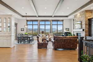 Living area with beam ceiling, light wood-style floors, a stone fireplace, and recessed lighting