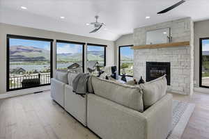 Living room featuring light wood finished floors, a stone fireplace, recessed lighting, vaulted ceiling, and a ceiling fan