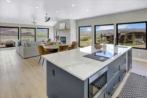 Kitchen featuring stainless steel microwave, recessed lighting, a center island with sink, light stone countertops, and light wood-style flooring