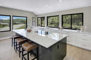 Kitchen featuring white cabinets, a kitchen island with sink, recessed lighting, light stone countertops, and lofted ceiling