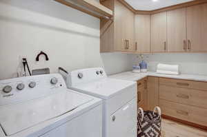 Washroom with cabinet space, washer and clothes dryer, and light wood-style floors