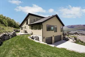 View of property exterior with a mountain view, an attached garage, a yard, concrete driveway, and a patio