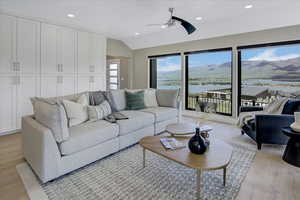 Living room featuring a water view, light wood-type flooring, lofted ceiling, recessed lighting, and ceiling fan