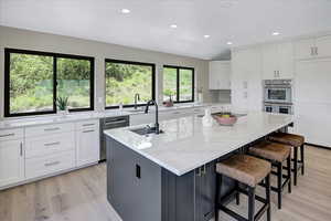 Kitchen with white cabinetry, recessed lighting, light stone countertops, a kitchen island with sink, and appliances with stainless steel finishes