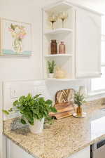 Kitchen view of backsplash, light stone counters, white cabinetry, and open shelves