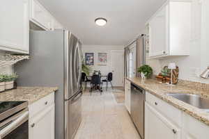 Kitchen featuring decorative backsplash, white cabinetry, light tile patterned floors, appliances with stainless steel finishes, and light stone countertops