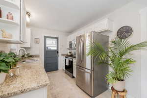 Kitchen with appliances with stainless steel finishes, white cabinetry, open shelves, light stone counters, and light tile patterned floors