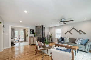 Living room featuring light wood-style floors, a wood stove, recessed lighting, french doors, and a ceiling fan