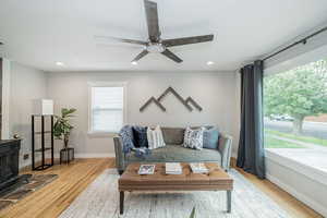 Living room with a wood stove, light wood-style floors, recessed lighting, and a ceiling fan