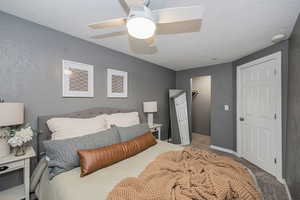 Bedroom featuring a textured wall, carpet flooring, a textured ceiling, ceiling fan, and a spacious closet