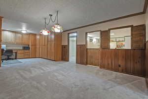 Unfurnished dining area with built in desk, wood walls, wainscoting, crown molding, and light carpet