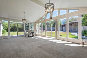 Sunroom / solarium featuring a chandelier, high vaulted ceiling, and carpet