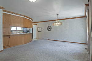 Kitchen with wallpapered walls, light carpet, open floor plan, ornamental molding, and pendant lighting