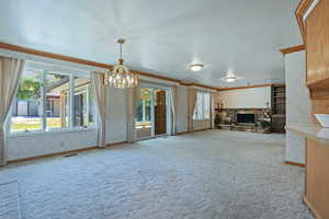 Unfurnished living room with light colored carpet, crown molding, a fireplace, and a chandelier