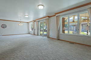 Unfurnished room with a chandelier, carpet flooring, and crown molding
