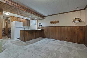 Kitchen with a wainscoted wall, wooden walls, freestanding refrigerator, brown cabinetry, and light countertops