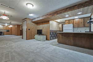 Kitchen with open floor plan, brown cabinets, light carpet, wooden walls, and freestanding refrigerator