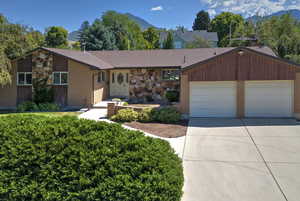 View of front facade with a mountain view, a garage, concrete driveway, brick siding, and stone siding