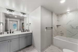 Bathroom featuring light marble finish floors, double vanity, washtub / shower combination, and recessed lighting